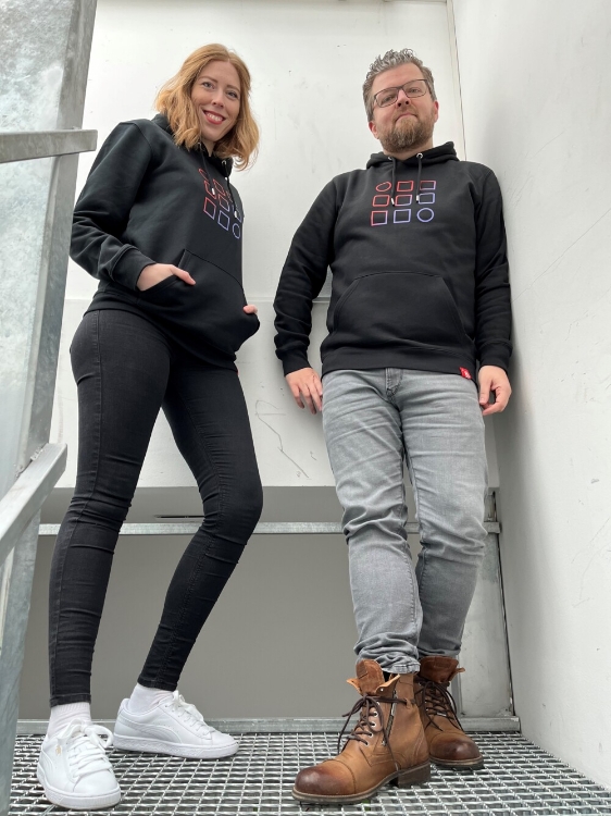 Männliches und weibliches Model tragen schwarzen Hoody mit Kapuze und buntes Logo auf der Vorderseite