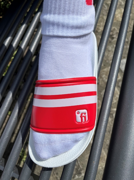 Badelatsche mit Fuß in weißer Socke, weiße Sohle, Brücke in weiß/rot gestreift mit Finanz Informatik Logo